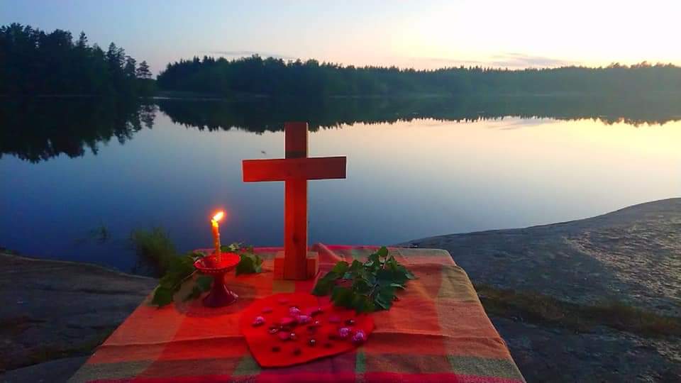 Lähetysilta Myllyjärvellä Alttaripöydällä puinen risti ja kukat vasten Myllyjärven rantamaisemaa.